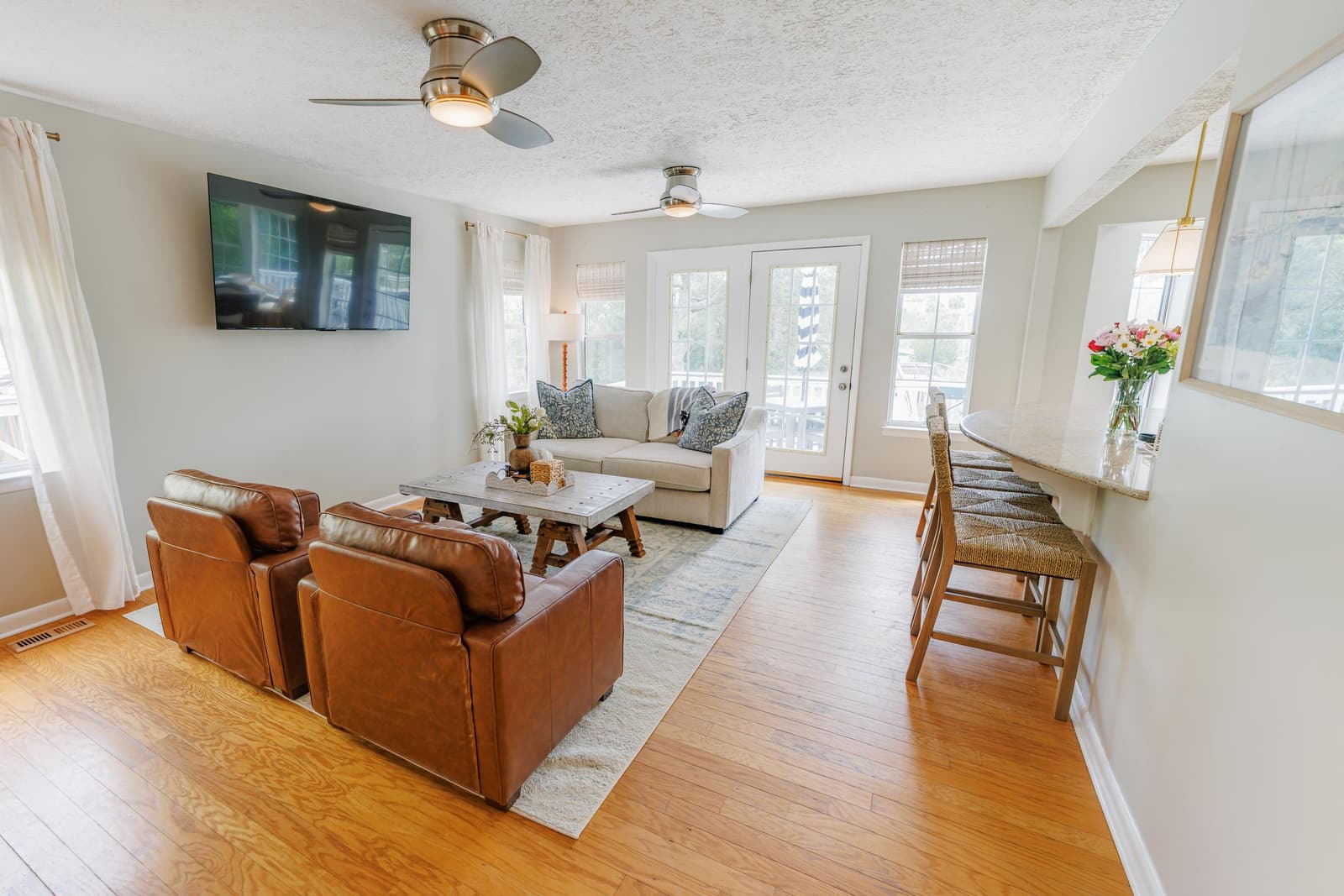 Second living room with a TV, leather chairs, and a counter with stools by the French doors