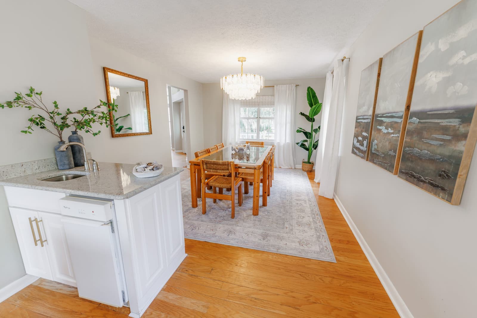 Dining table with wood chairs and a chandelier, seen from the kitchen