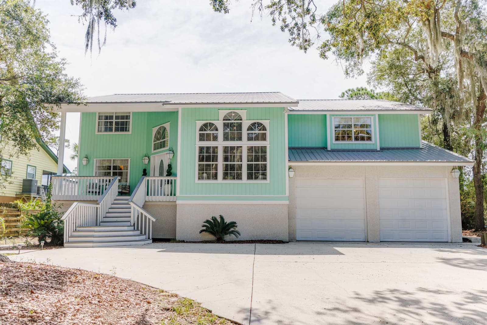 Front of the Retreat at San Marco: seafoam board siding, a triple arched window wall, and a double staircase up to the porch