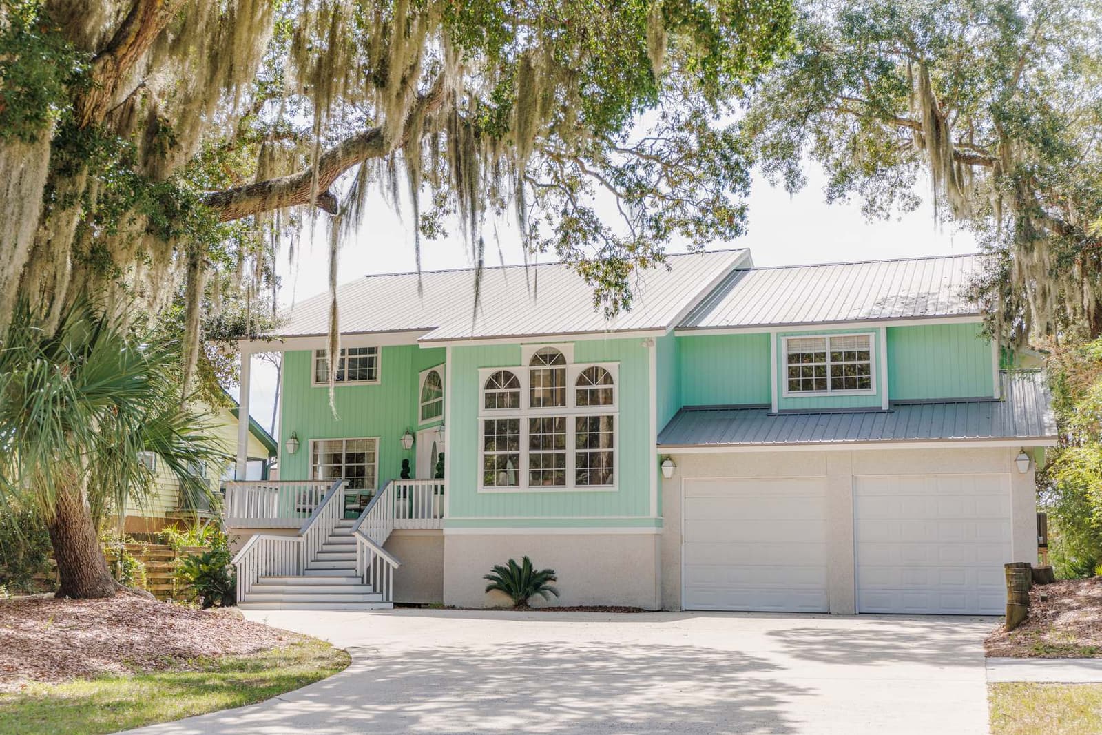 Seafoam-green front of the house with a two-car garage and driveway under Spanish moss