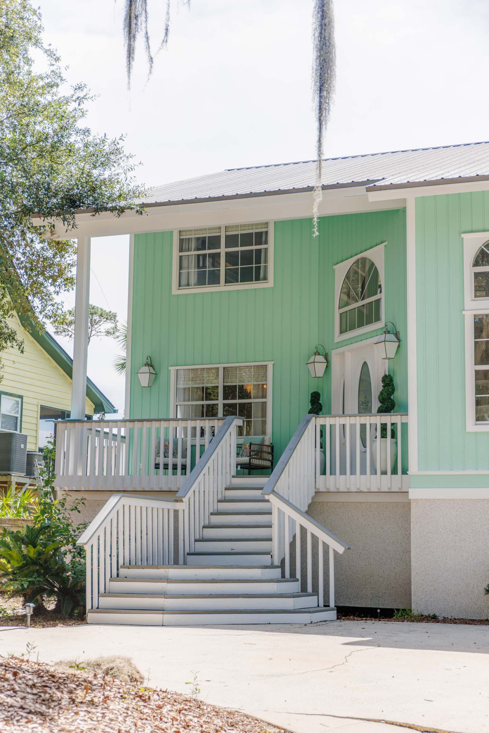 Front porch and white-railed staircase against the seafoam siding, with a lantern by the front door