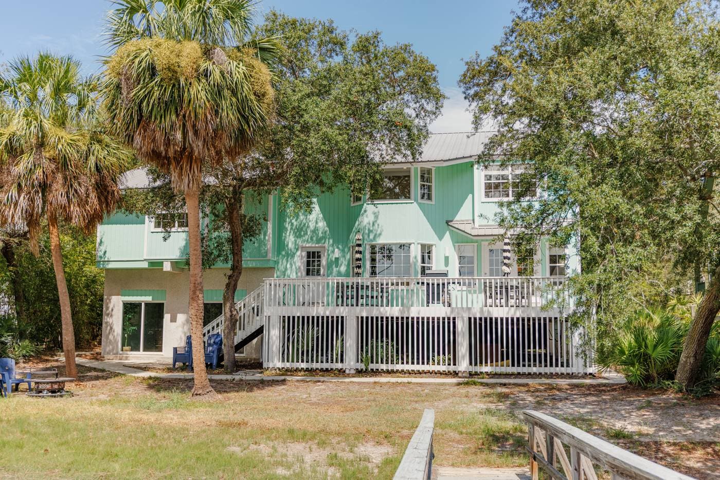 Back of the house with a raised deck, white railings, and palms across the back lawn