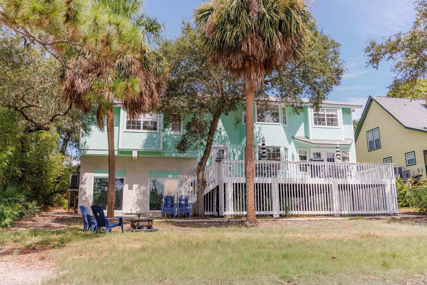 Rear deck and lawn with palm trees and two blue Adirondack chairs