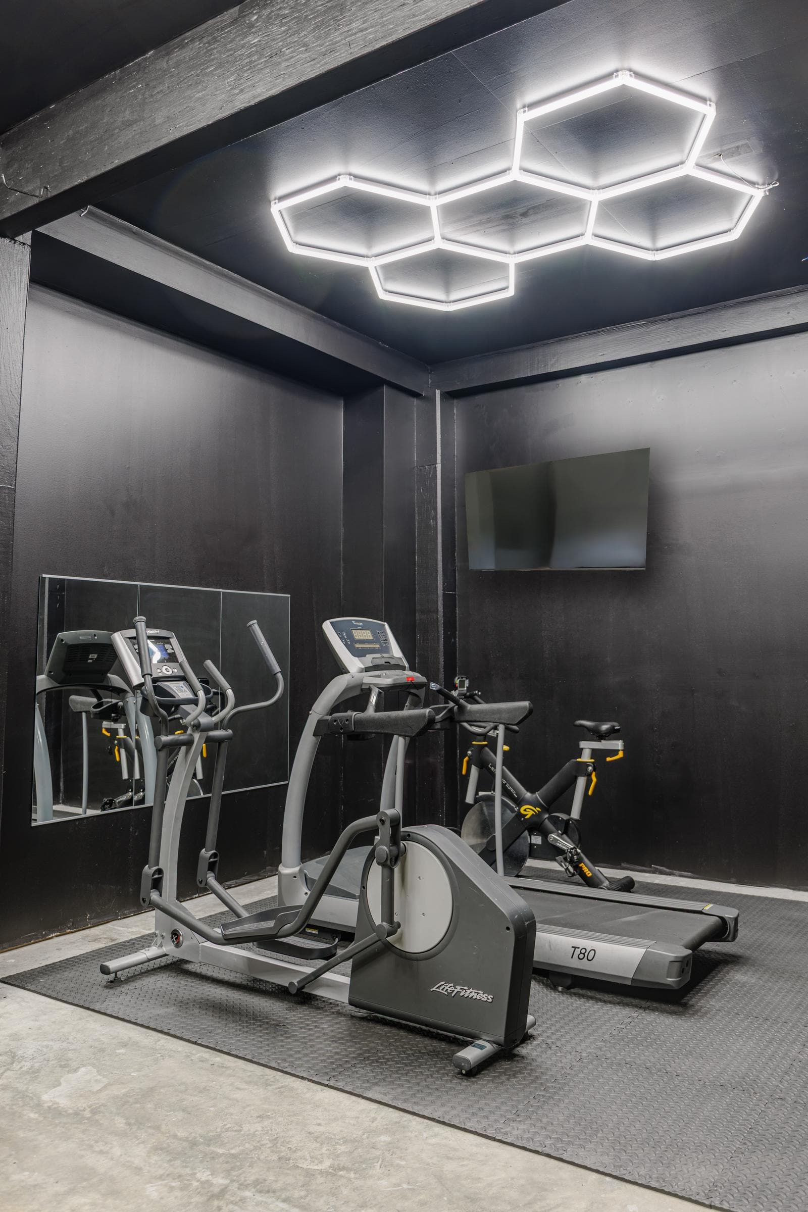 Garage gym with a black accent wall, elliptical machines, and an exercise bike