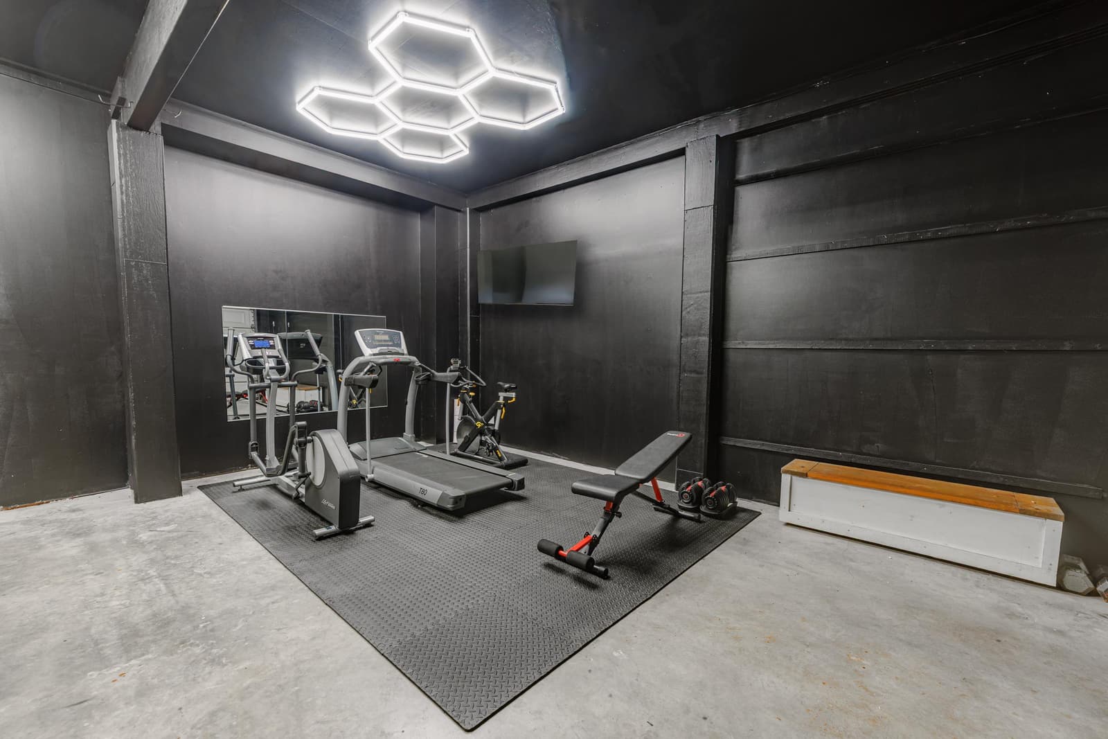 Garage gym with a treadmill, bench, and hexagon ceiling lights