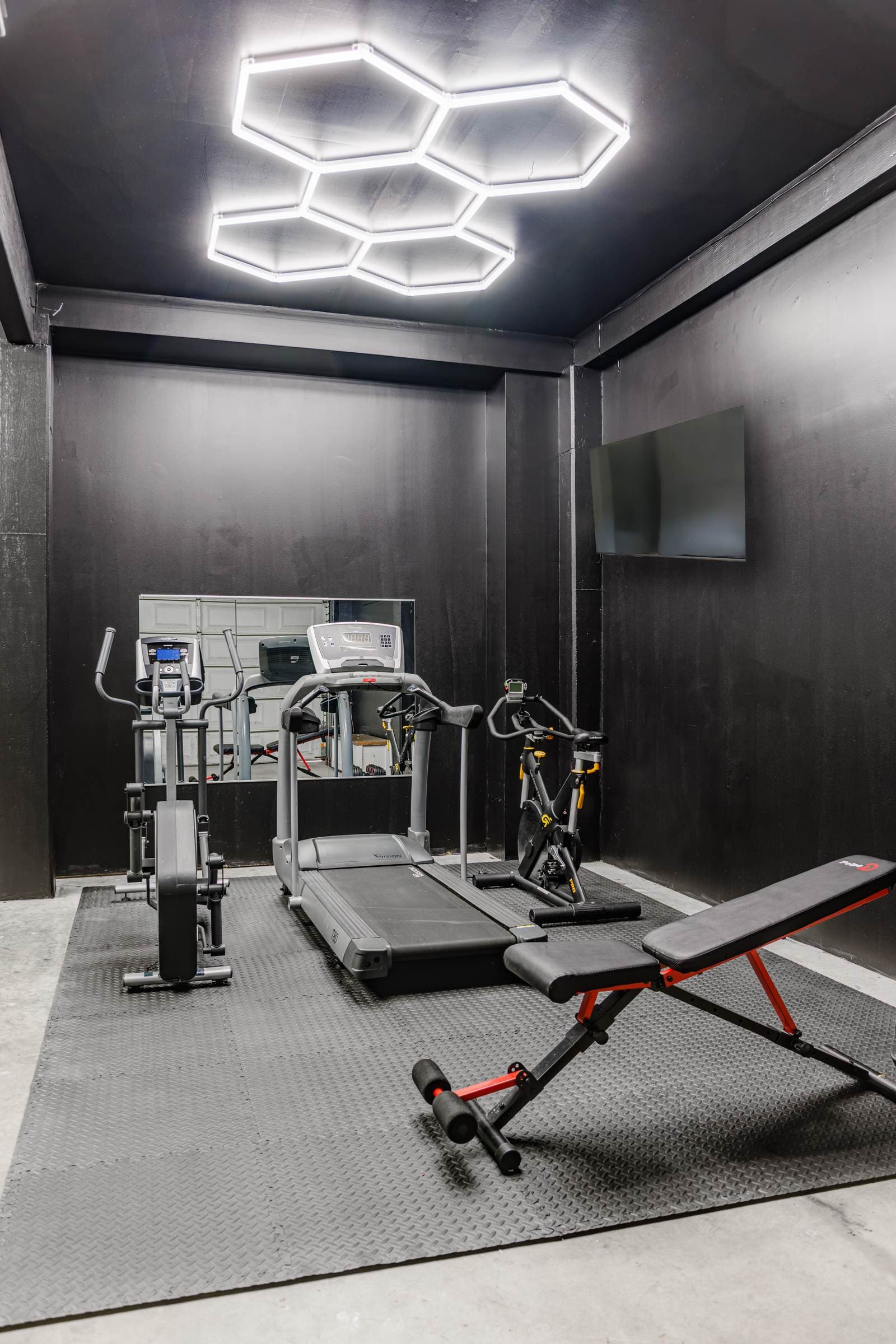 Garage gym with a treadmill, elliptical, and adjustable bench