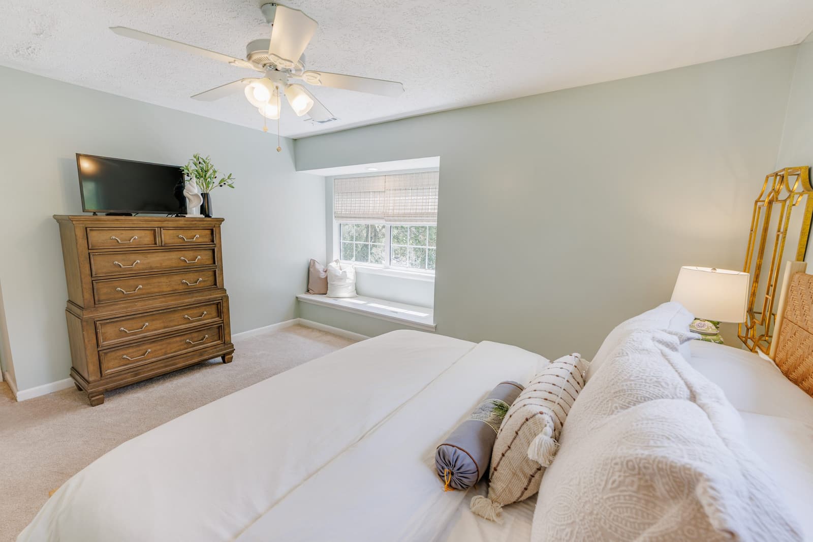 Classic guest bedroom with a TV on a wood dresser and a window seat