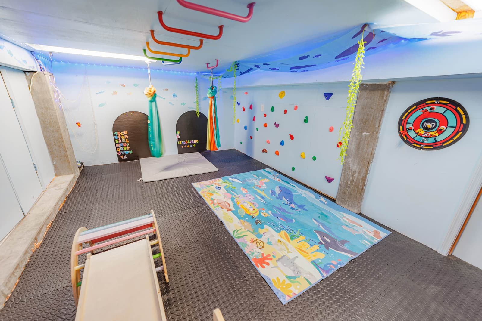 Kids' hideout room with a rock wall, monkey bars, and a colorful play rug