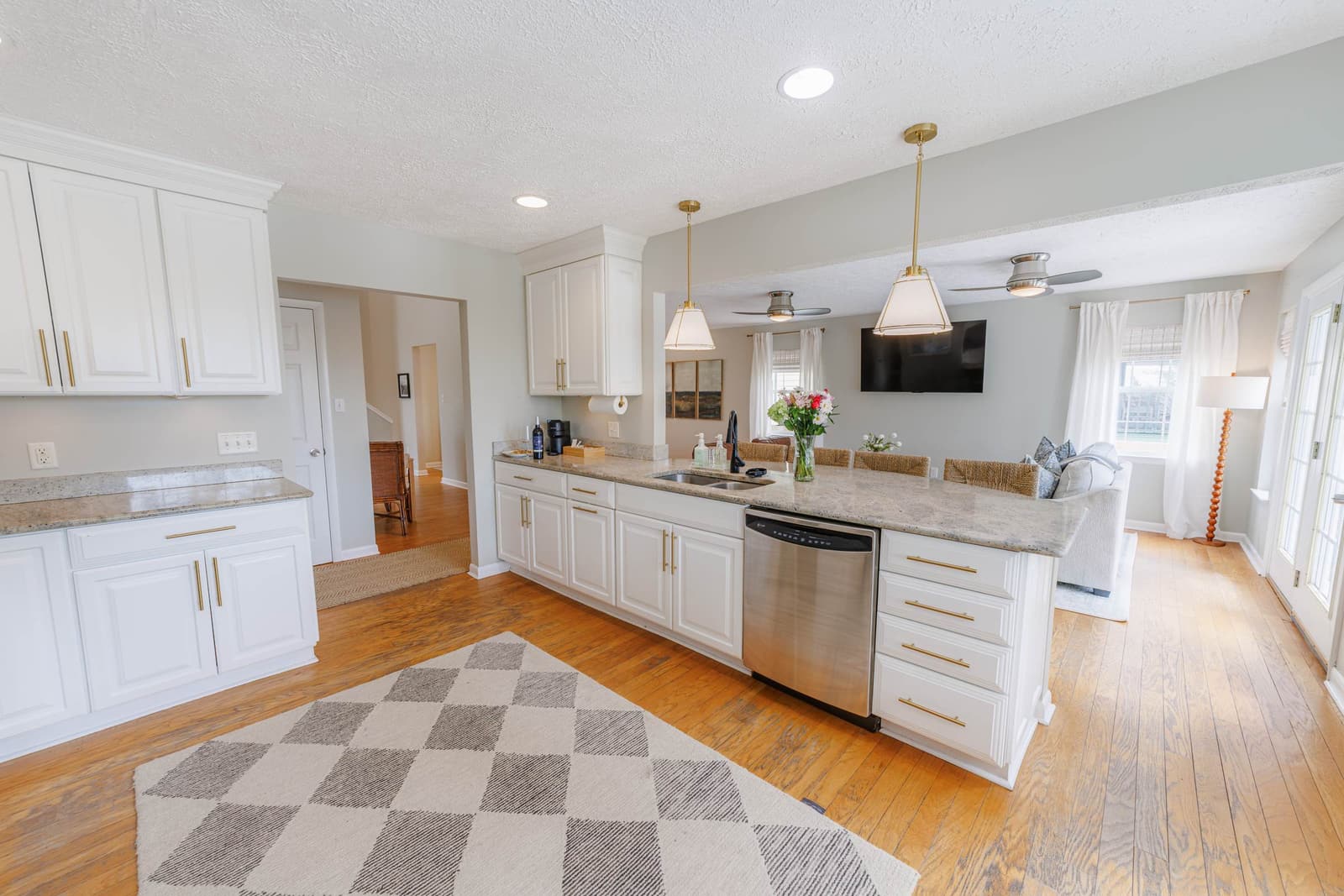 Long kitchen counter with a dishwasher and pendant lights, open to the second living room