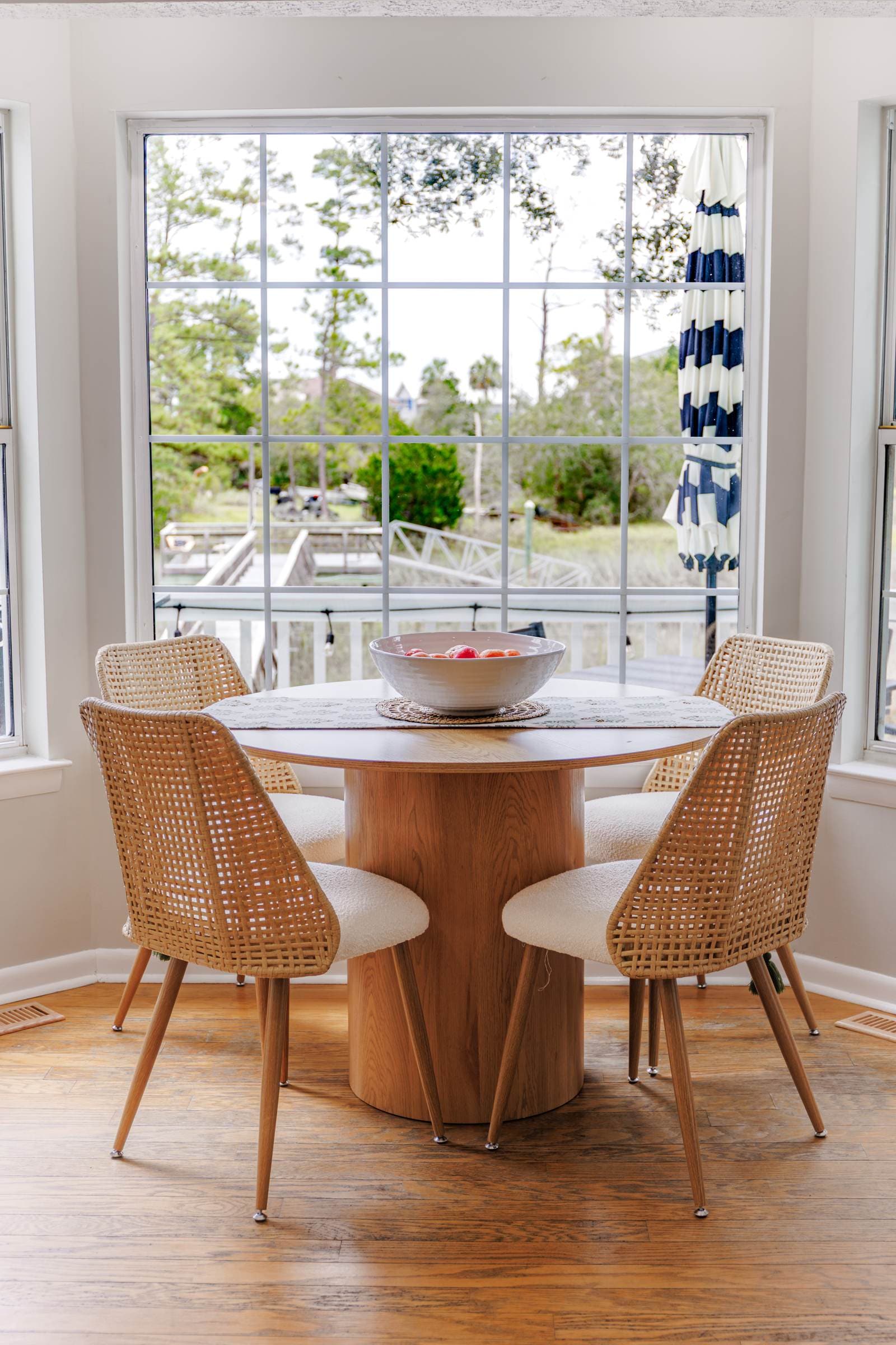 Round breakfast table with woven chairs beside a window over the back deck