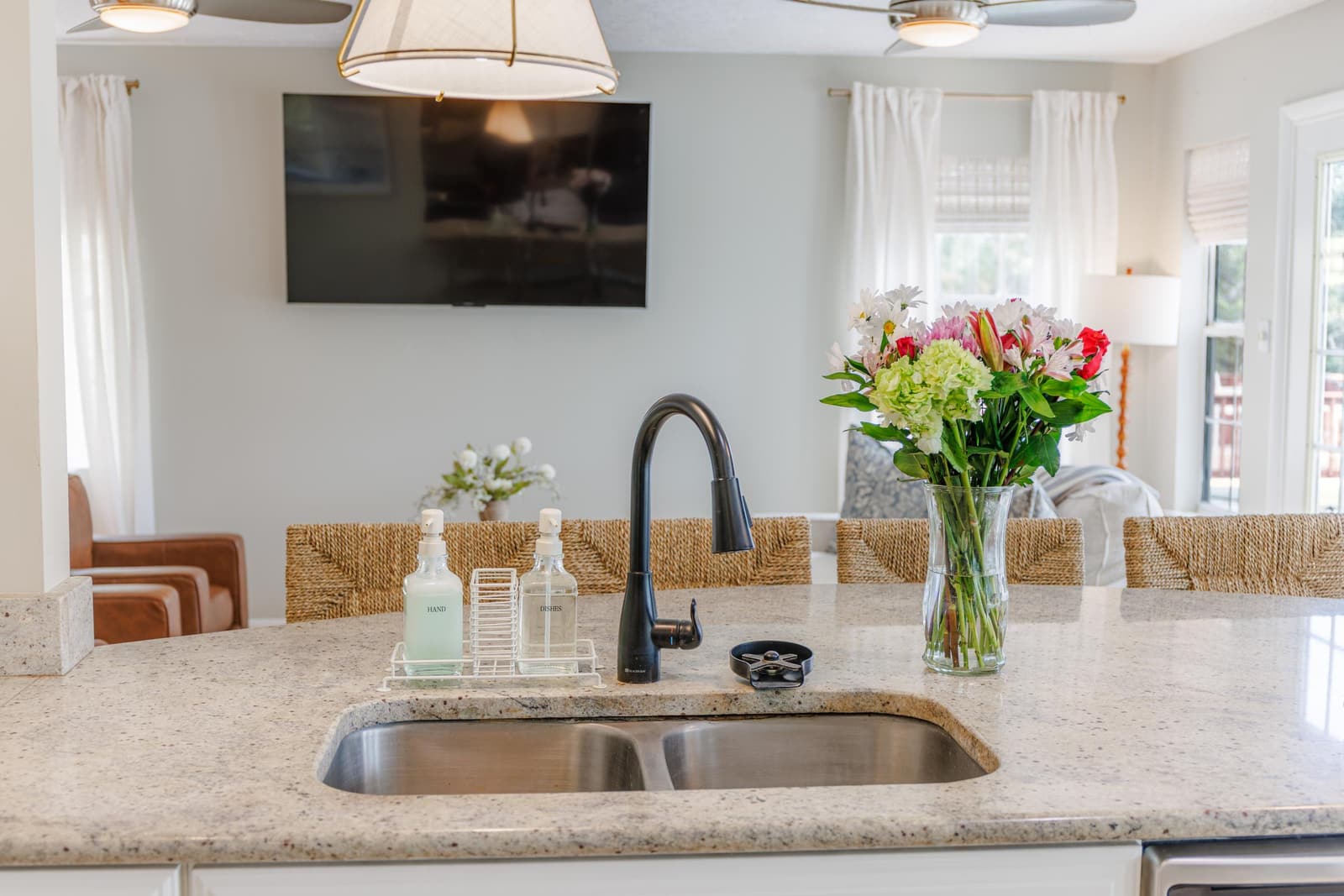 Kitchen sink with a black faucet and fresh flowers, with the TV area beyond