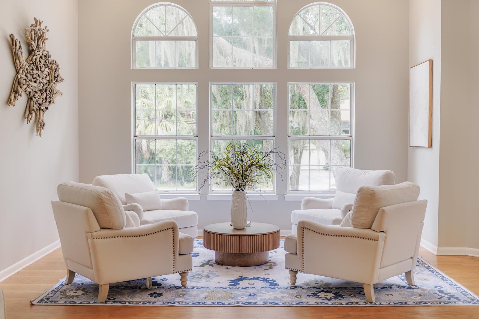 Living room seating area in front of tall arched windows, with cream armchairs and a blue rug