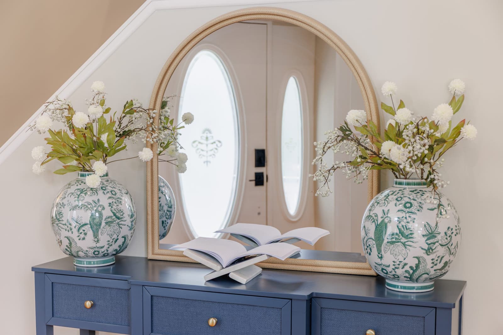 Entry console with a large arched mirror and green-and-white vases beside the front doors