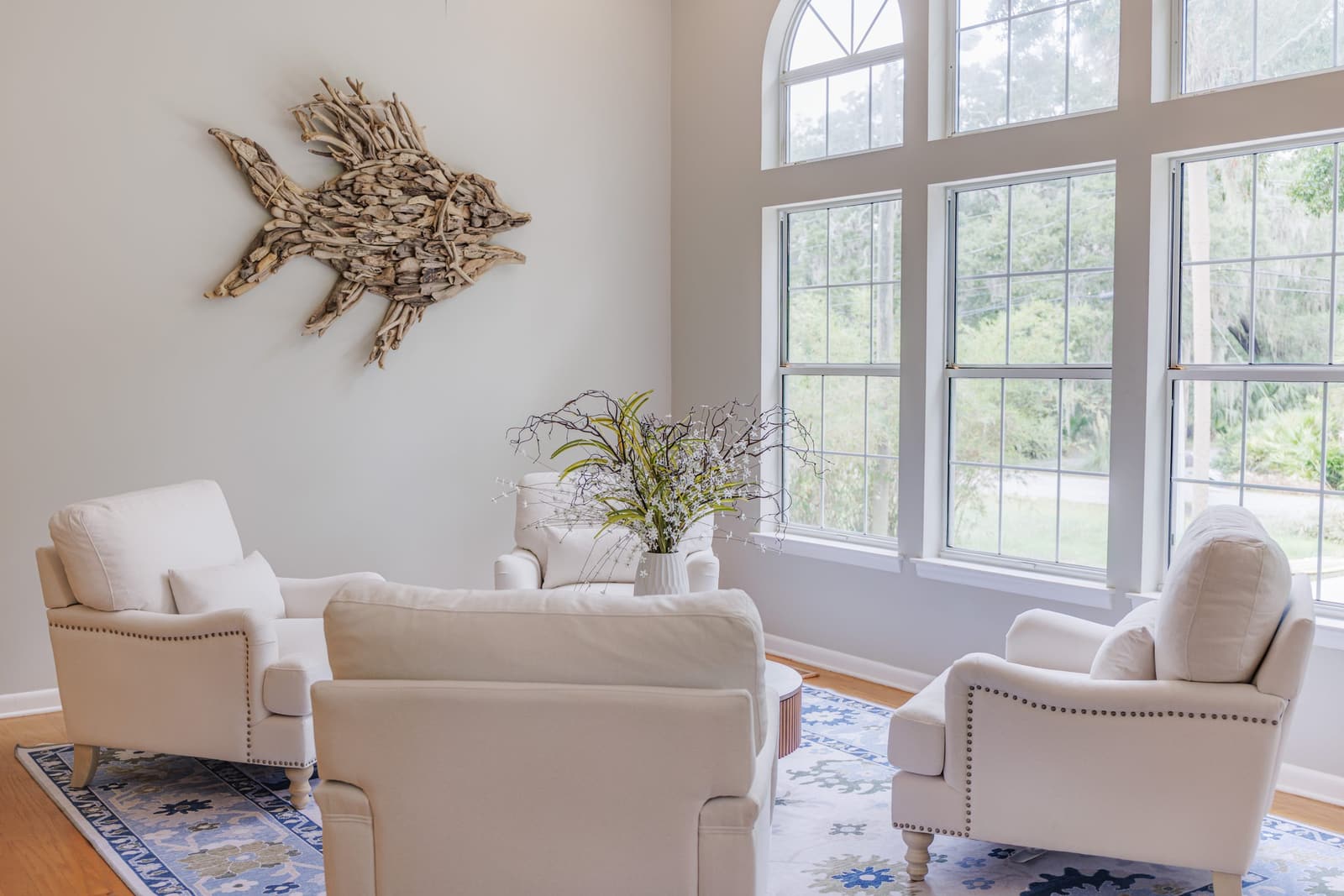 Living room sofa and armchairs beside tall windows, with a driftwood fish on the wall