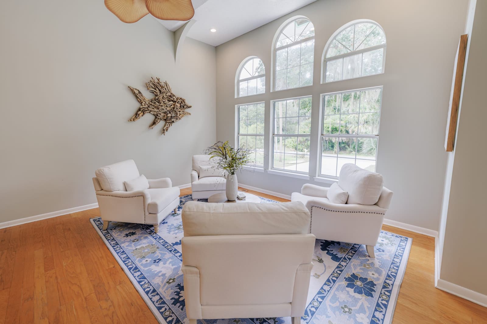 Living room seating group facing the arched windows, with a driftwood fish on the wall