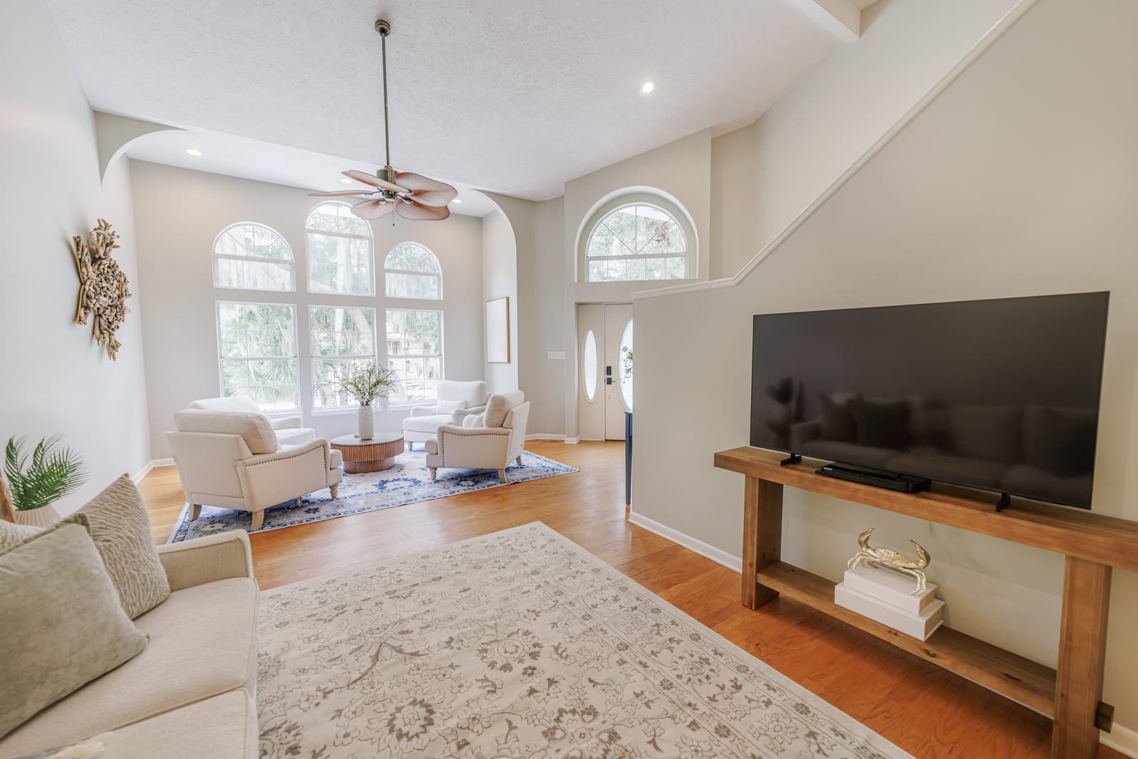 Living room with a large TV on a wood console, ceiling fans, and an area rug