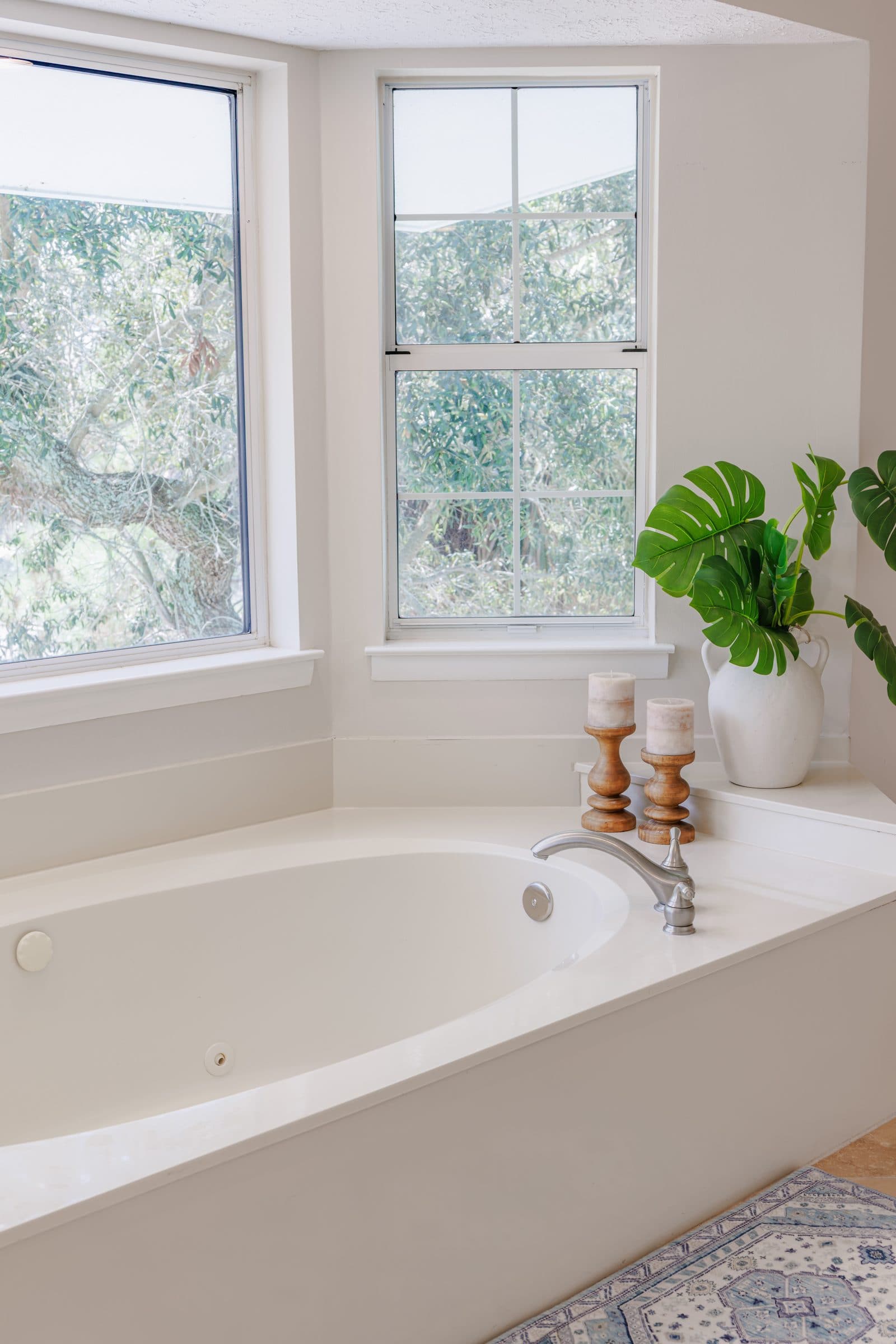 Soaking tub in the primary bath beside a window, with candles and a plant