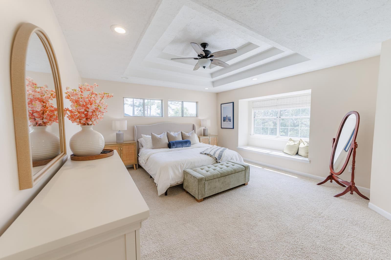 Primary suite with a tray ceiling, king bed, green tufted bench, and dresser