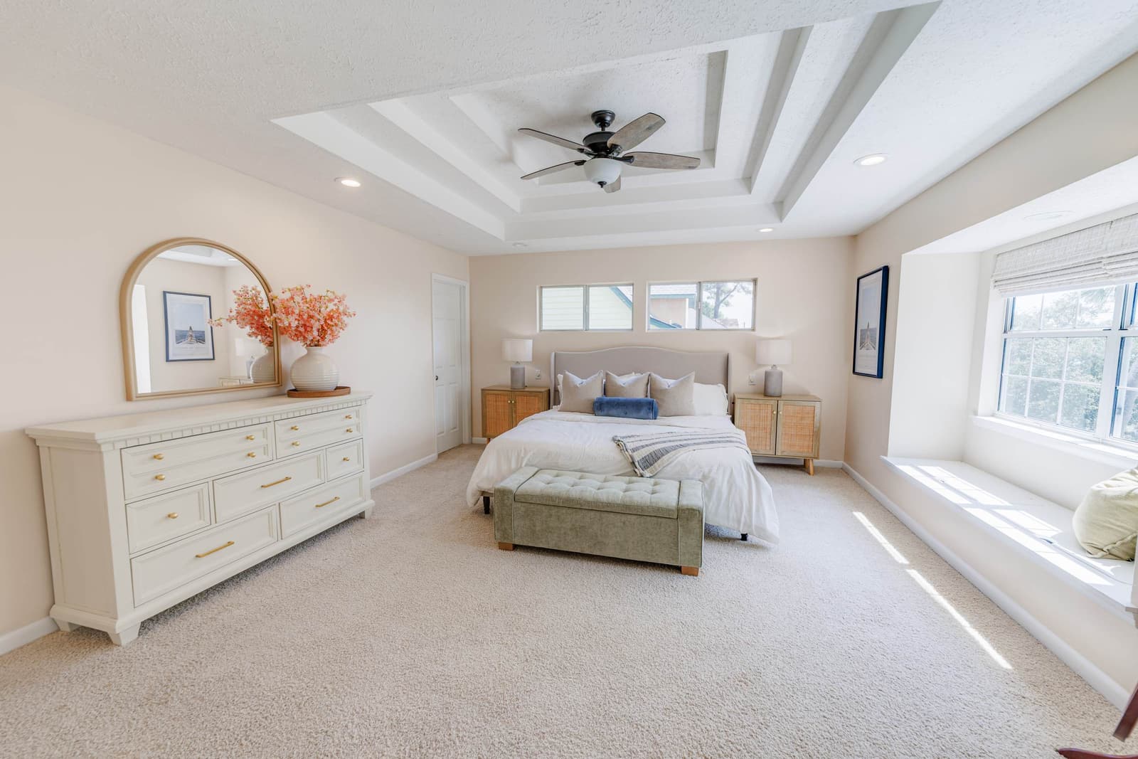 Primary suite bed and dresser under a tray ceiling, with a window bench