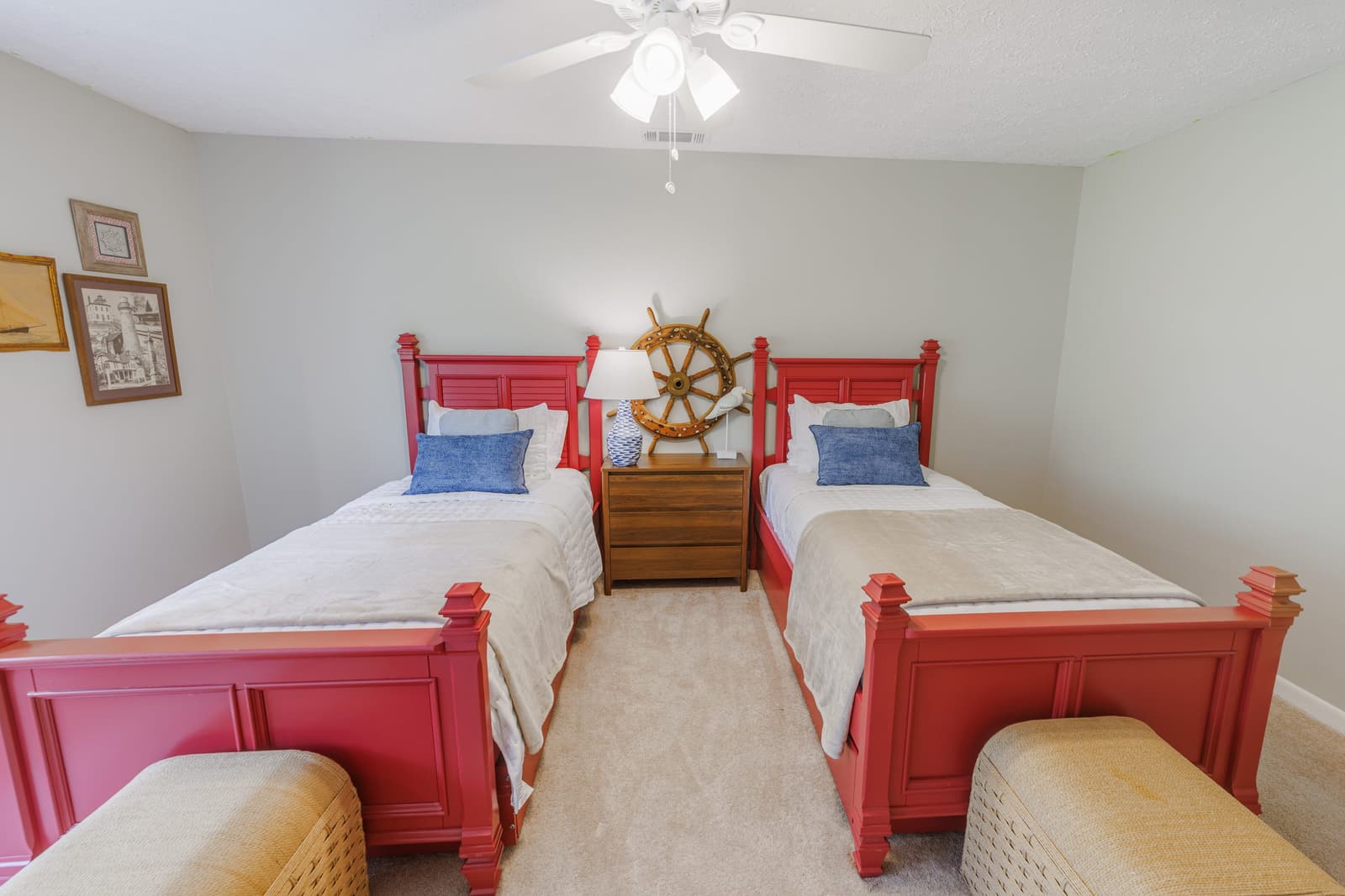 Two red twin beds with a ship's wheel above and woven ottomans