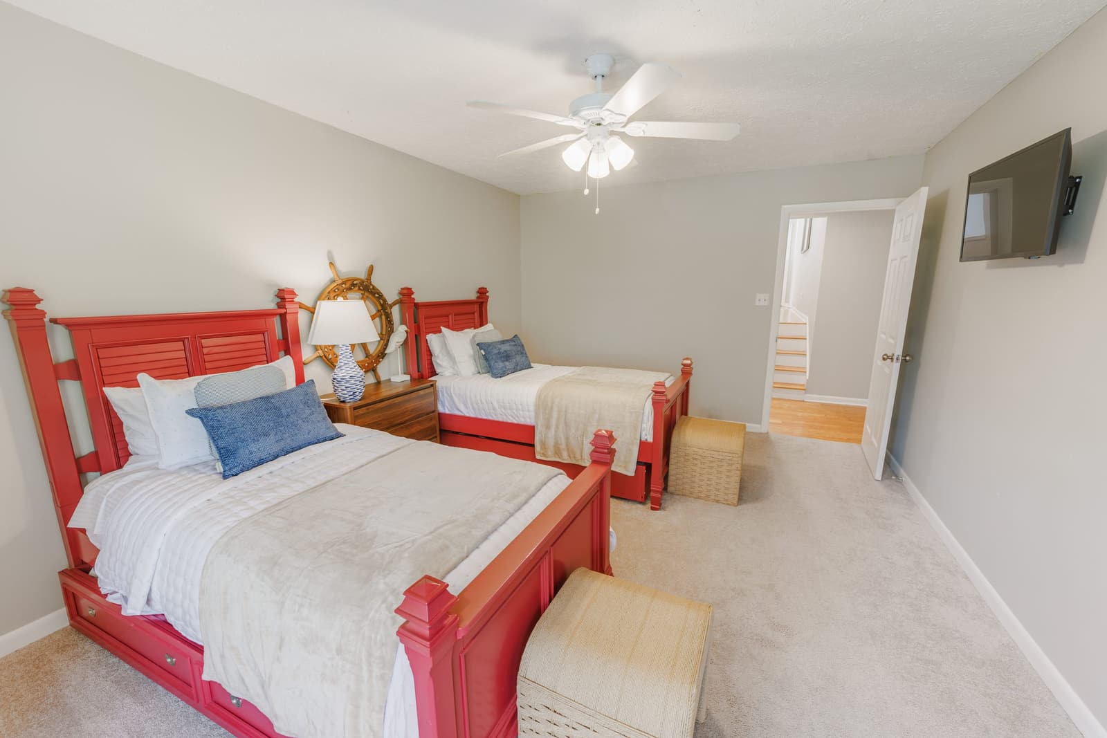 Twin bedroom with red bed frames, blue pillows, and a ship's wheel on the wall