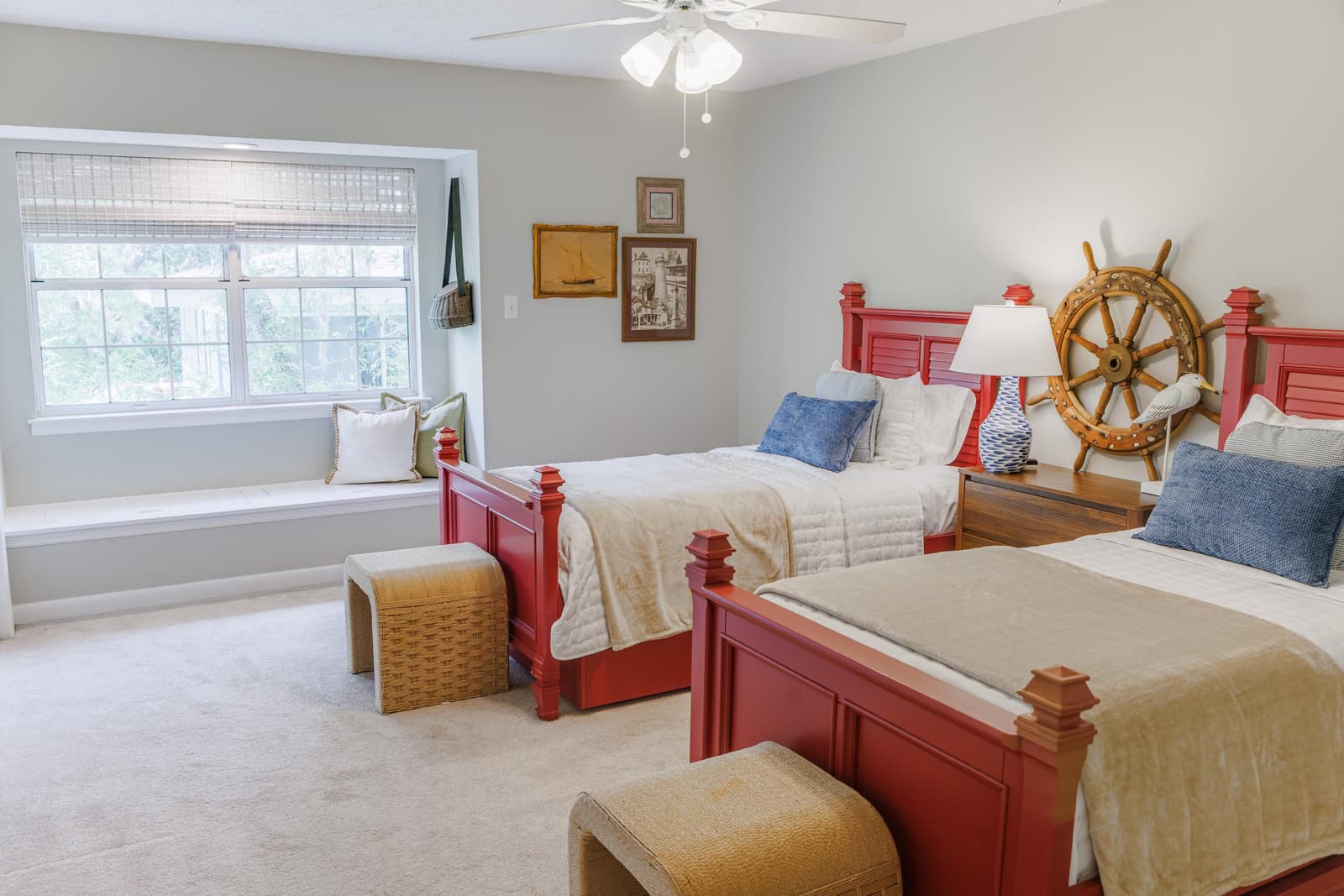 Twin bedroom with red bed frames, a ship's wheel, and a window bench